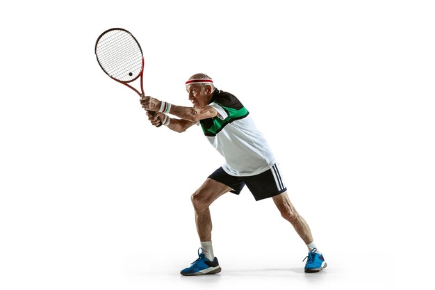 Hombre senior jugando al tenis en ropa deportiva aislado en la pared blanca