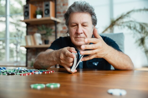 Hombre senior jugando a las cartas y bebiendo vino con amigos, parece feliz