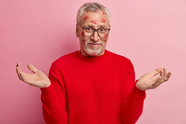 Hombre senior con manchas de lápiz labial en la cara y vistiendo un suéter rojo