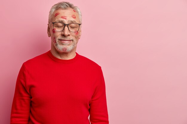 Hombre senior con manchas de lápiz labial en la cara y vistiendo un suéter rojo