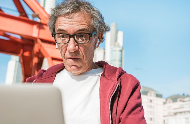 Hombre senior sorprendido con lentes negras mirando portátil