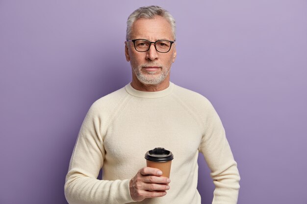 Hombre senior en suéter blanco y anteojos sosteniendo la taza de café