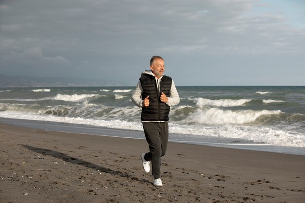 Hombre senior de tiro completo corriendo en la playa