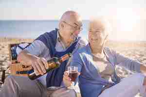 Foto gratuita hombre senior vertiendo vino tinto en la playa, la jubilación y el concepto de vacaciones de verano