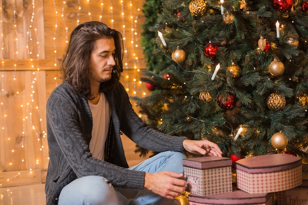 Hombre sentado al lado de árbol de navidad