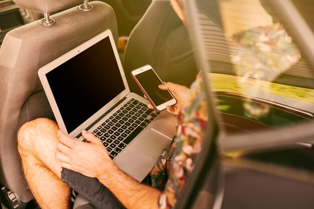 Hombre sentado en auto con laptop y smartphone