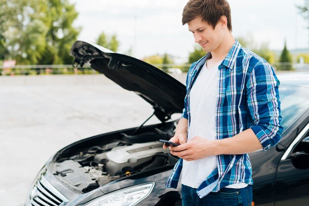 Hombre sentado en el auto y revisando el teléfono