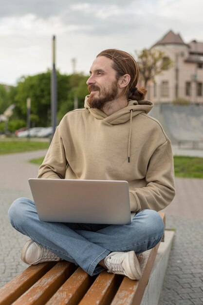 Hombre sentado en el banco de la ciudad y trabajando en la computadora portátil