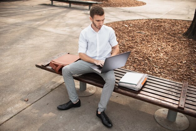 Hombre sentado en el banco y trabajando en la computadora portátil