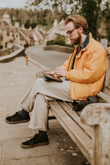 Hombre sentado en un banco y trabajando en tableta en el pueblo