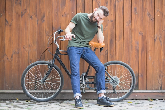 Hombre sentado en bicicleta contra la pared de madera