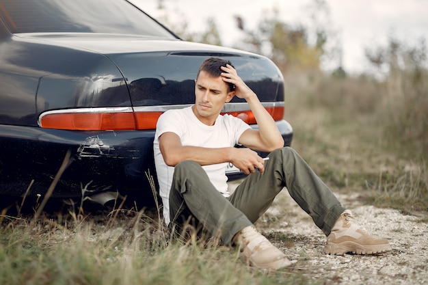 Foto gratuita hombre sentado cerca del auto roto