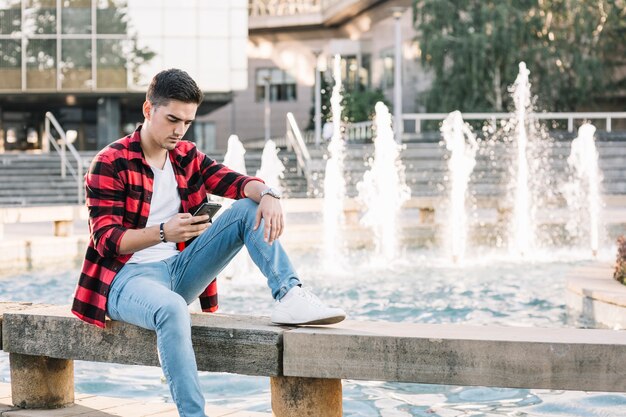 Hombre sentado cerca de fuente usando teléfono celular