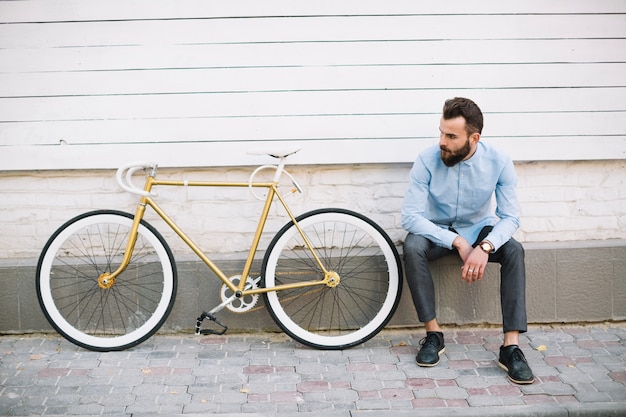 Hombre sentado cerca de la pared blanca y la bicicleta