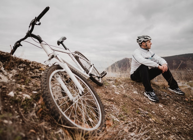 Hombre sentado en el césped junto a su bicicleta de montaña