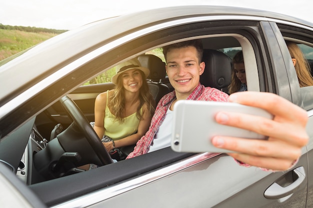 Hombre sentado en el coche con su novia tomando selfie en smartphone