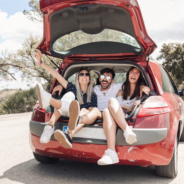 Hombre sentado con dos amigas en el maletero del coche