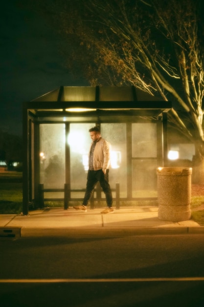 Hombre sentado en la estación de autobuses por la noche en la ciudad