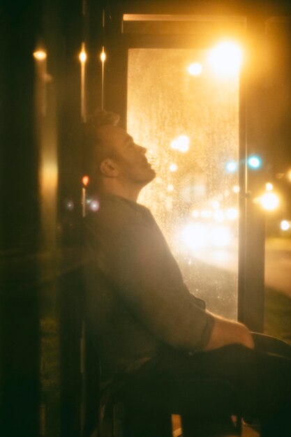 Hombre sentado en la estación de autobuses por la noche en la ciudad