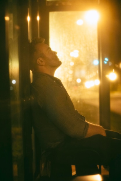 Hombre sentado en la estación de autobuses por la noche en la ciudad