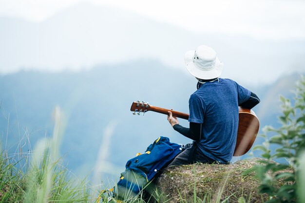 Un hombre sentado felizmente tocando la guitarra en el bosque solo.