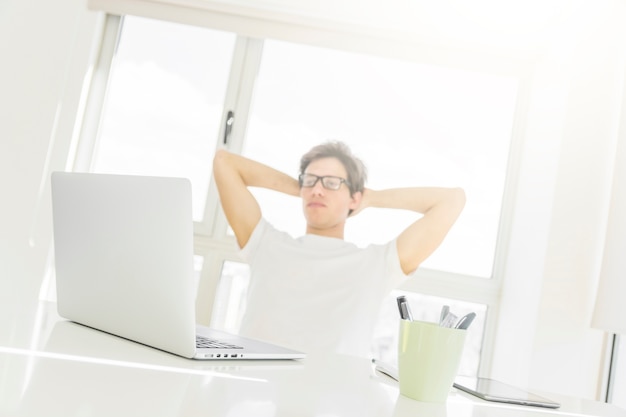 Hombre sentado frente a la computadora portátil con las manos detrás de la cabeza