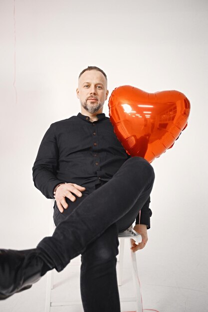 Hombre sentado frente a un montón de globos rojos en forma de corazón posando en el estudio