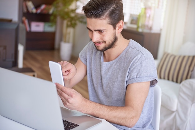 Hombre sentado frente a su escritorio y usando un teléfono inteligente