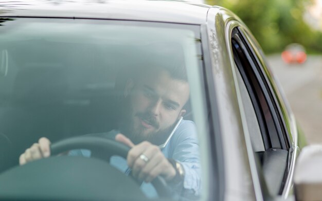 Hombre sentado en el interior del coche hablando por teléfono móvil visto a través del parabrisas