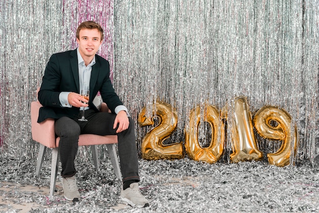 Hombre sentado junto a globos dorados fiesta de año nuevo