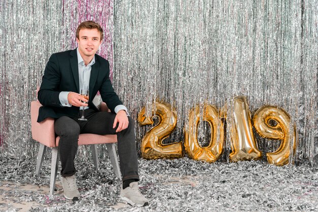 Hombre sentado junto a globos dorados fiesta de año nuevo