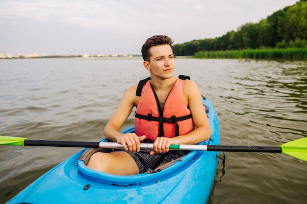 Foto gratuita hombre sentado en kayak sosteniendo paleta apartar la mirada