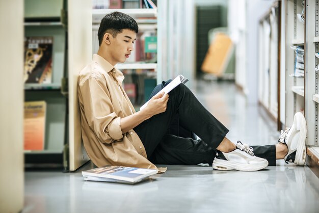 Un hombre sentado leyendo un libro en la biblioteca.