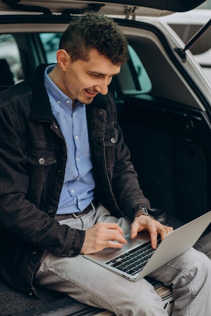 Hombre sentado en el maletero de su coche y trabajando en la computadora