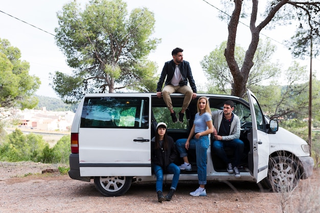 Foto gratuita hombre sentado en la parte superior del coche con amigos