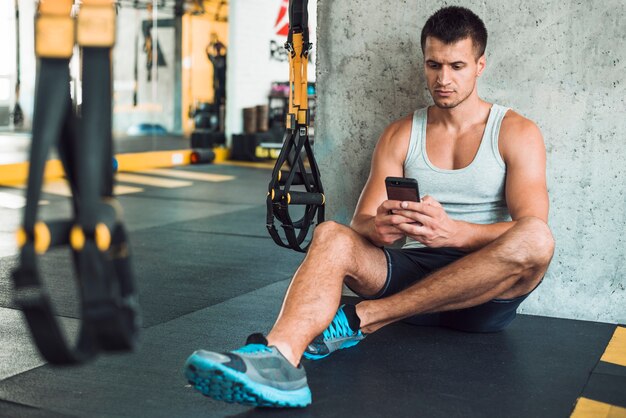 Hombre sentado en el piso usando el teléfono móvil en el gimnasio