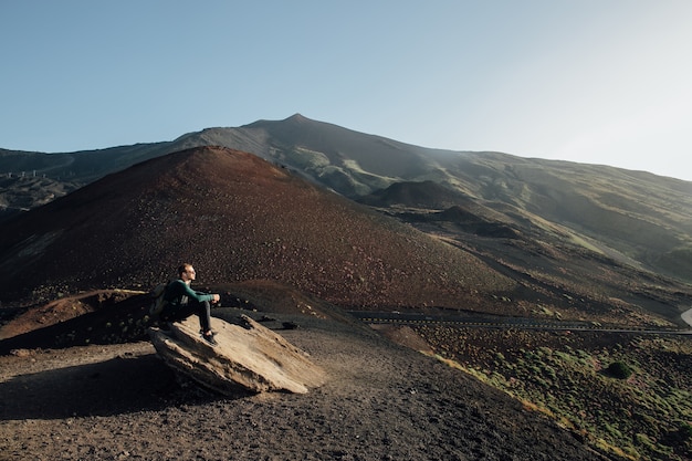 Hombre sentado en la roca y disfrutando del hermoso paisaje del volcán Etna en Sicilia