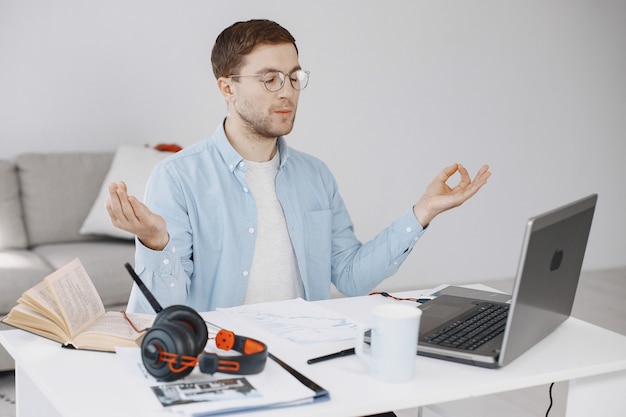 Hombre sentado en la sala de estar en casa. Chico disfruta estudiando con ordenador portátil y auriculares. Meditación.