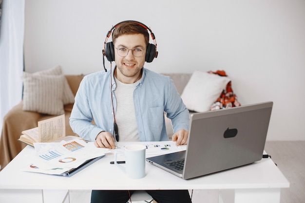 Hombre sentado en la sala de estar en casa. Chico disfruta estudiando con ordenador portátil y auriculares.