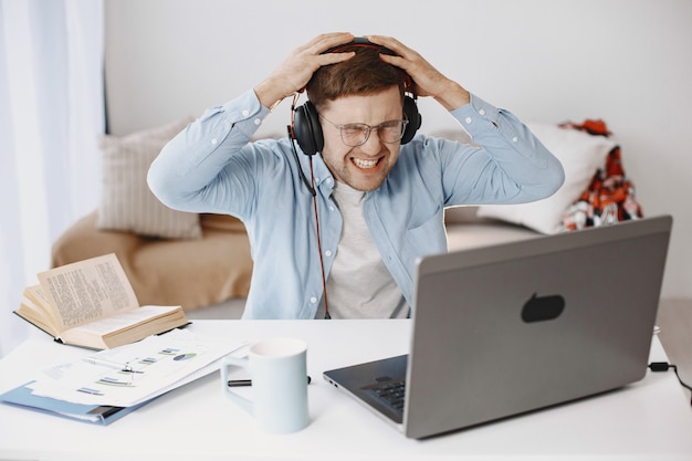 Hombre sentado en la sala de estar en casa. Chico disfruta estudiando con ordenador portátil y auriculares.