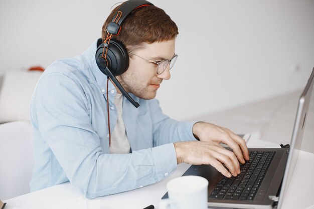 Hombre sentado en la sala de estar en casa. Chico disfruta estudiando con ordenador portátil y auriculares.