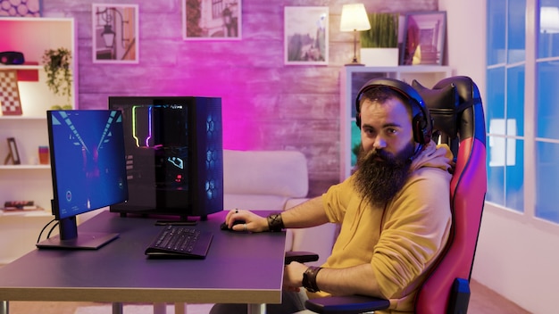 Hombre sentado en una silla de juego y jugando videojuegos en su habitación con coloridos neones usando audífonos.
