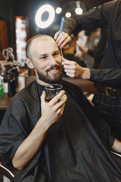 Hombre sentado en una silla. Peluquería con cliente. Guy bebiendo un whisky.