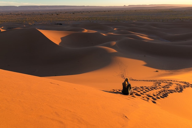 Hombre sentado sobre las dunas de arena rodeado de pistas en un desierto