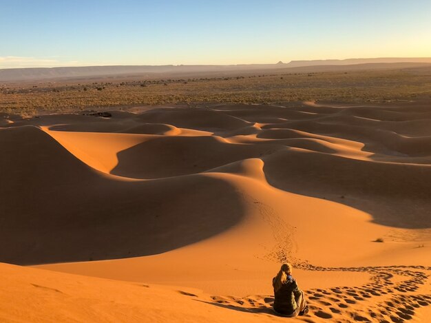 Hombre sentado sobre las dunas de sol en un desierto rodeado de pistas