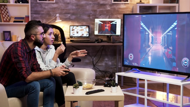 Hombre sentado en el sofá jugando videojuegos en la televisión con su novia junto a él.