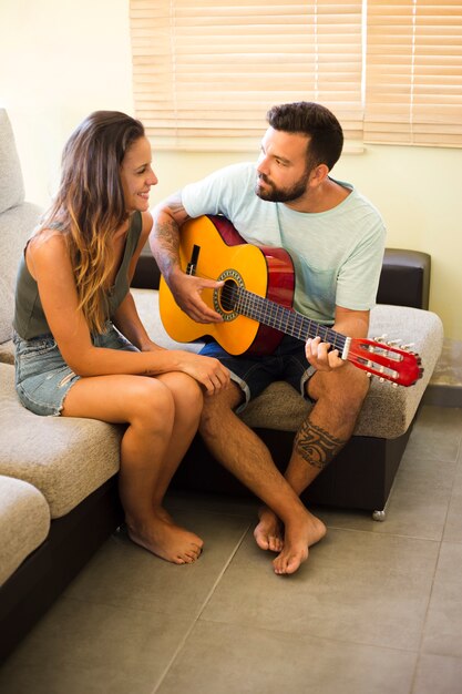 Hombre sentado en el sofá tocando la guitarra para su esposa