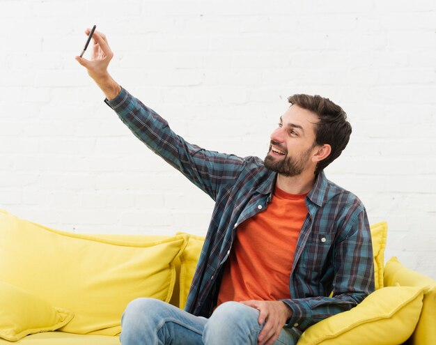 Hombre sentado en el sofá y tomando selfies