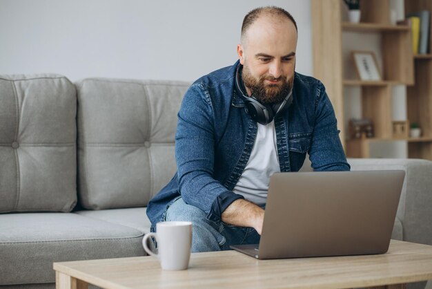 Hombre sentado en el sofá y trabajando desde casa en su computadora portátil