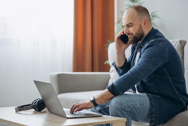 Hombre sentado en el sofá y trabajando desde casa en su computadora portátil